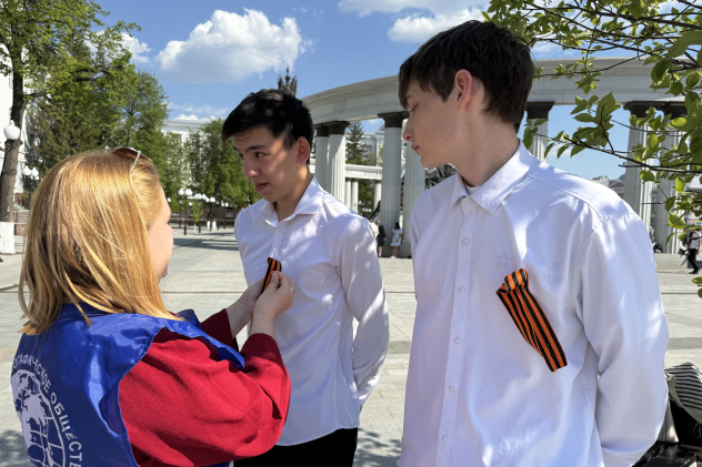 Волонтёр вручает георгиевские ленточки молодым людям Волонтёр вручает георгиевские ленточки молодым людям