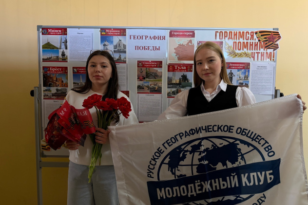 Участницы мероприятия с флагом Молодёжного клуба РГО и красными гвоздиками у стенда «География Победы» Участницы мероприятия с флагом Молодёжного клуба РГО и красными гвоздиками у стенда «География Победы»