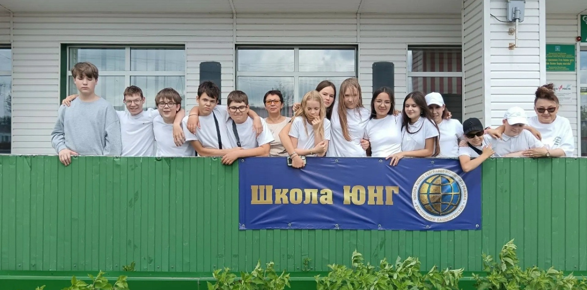 Участники лагеря с флагом РГО и баннером «Школа ЮНГ» на территории школы Участники лагеря с флагом РГО и баннером «Школа ЮНГ» на территории школы