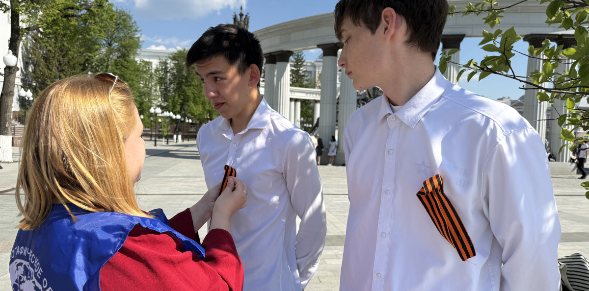 Волонтёр вручает георгиевские ленточки молодым людям