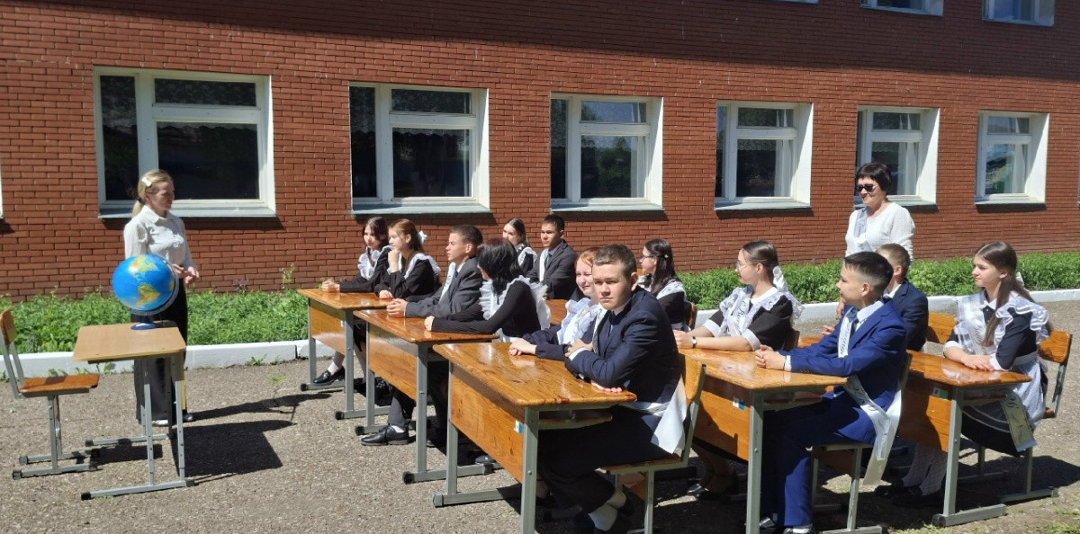 Педагог демонстрирует особенности глобуса учащимся на школьном дворе