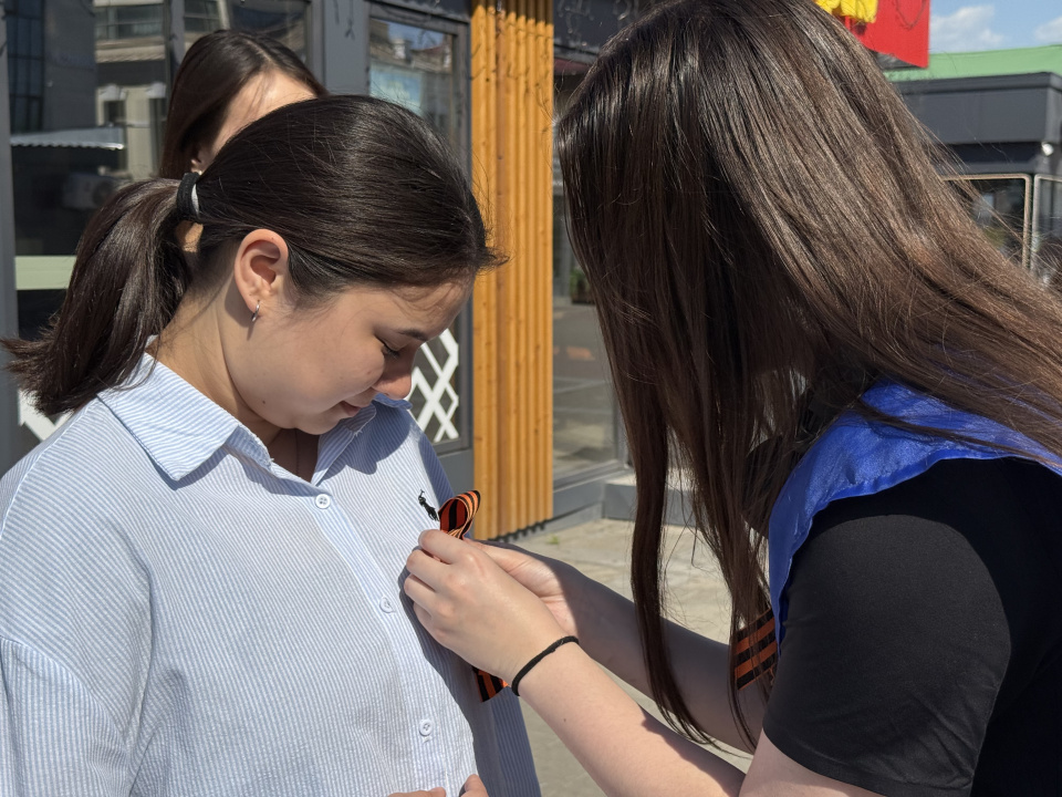 Активистка прикалывает георгиевскую ленточку жительнице города